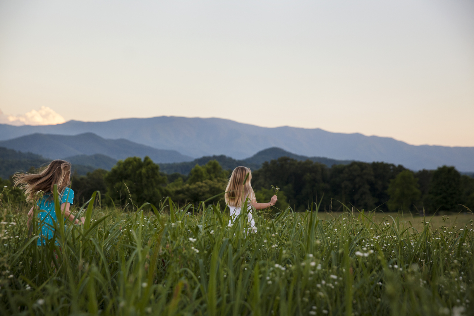 Children playing in a field with a view of the smoky mountains.