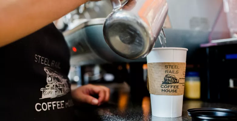 A barista pours hot water into Steel Rails Coffee cup.